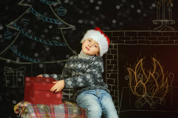 Menino em Santa chapéu no fundo de Natal com uma caixa vermelha. Feliz Natal — Fotografia de Stock
