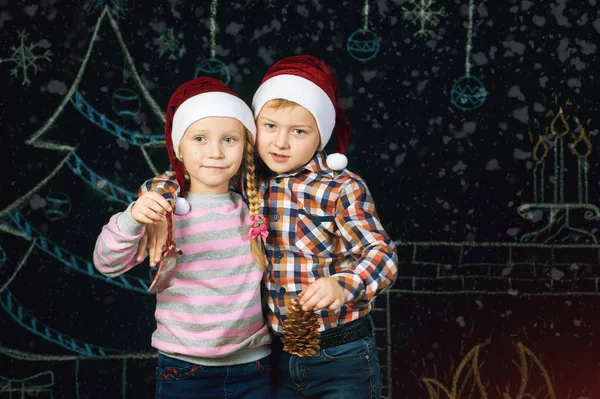 Jongen en meisje op Kerstmis achtergrond, Santa hoeden . — Stockfoto