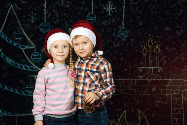 Хлопчик і дівчинка на різдвяному тлі, Санта-капелюхи  . — стокове фото