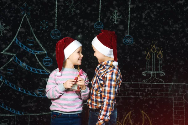 Jongen en meisje op Kerstmis achtergrond, Santa hoeden . — Stockfoto