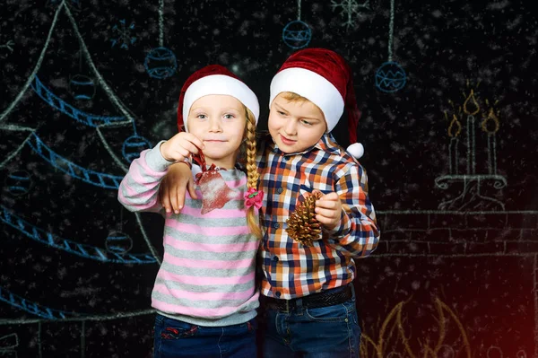 Мальчик и девочка на фоне Рождества, Санта шляпы  . — стоковое фото