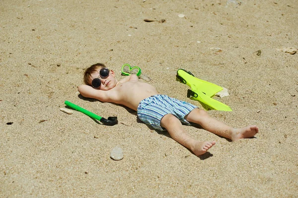 Niño feliz acostado en la playa en gafas del sol — Foto de Stock