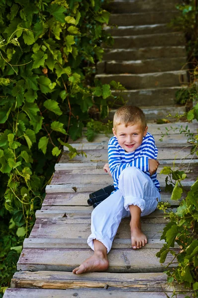 Bellissimo ragazzo in posa su una scala di legno. Vestita in stile nautico  . — Foto Stock