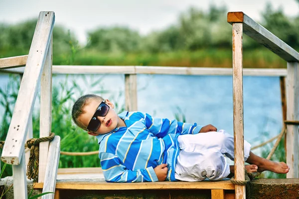 Bellissimo ragazzo in posa su un ponte di legno. Vestita in stile nautico — Foto Stock
