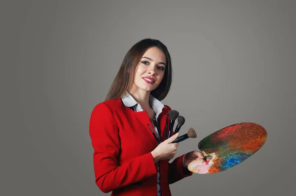 Веселая красивая молодая женщина визажистка на сером фоне, с палитрой в руке — стоковое фото