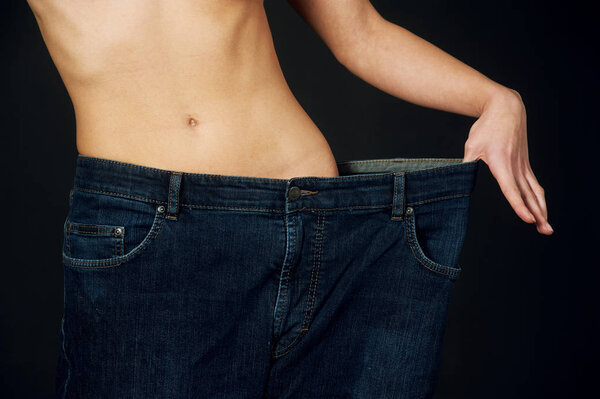 beautiful young woman with big jeans weight loss after the diet . On a dark background