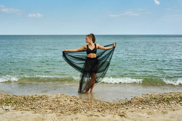 Молодая женщина в черном шифонском платье на берегу моря — стоковое фото