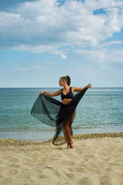 Jeune femme dans une robe en mousseline noire sur le bord de la mer — Photo