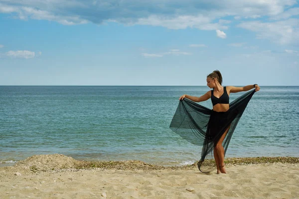 Jonge vrouw in een zwart chiffon jurk aan de kust — Stockfoto