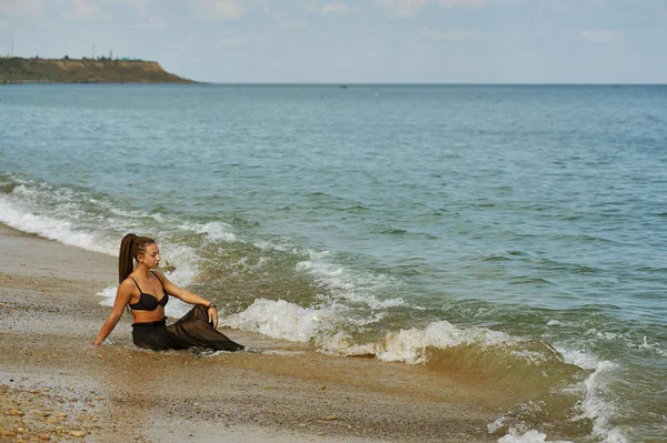 Jonge vrouw in een zwart chiffon jurk aan de kust — Stockfoto