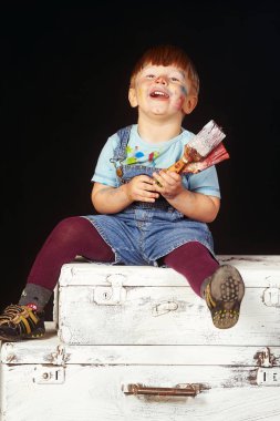 fırça ile küçük çocuk el, yüz ve eller boya ile bulaşmış. Karanlık bir arka plan üzerinde