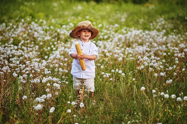 Un niño en un sombrero de paja con una barra de pan francés — Foto de Stock