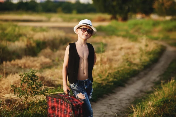 Stylově oblečený kluk v poli s kufrem — Stock fotografie