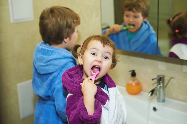 Kinderen poetsen hun tanden 's morgens in de badkamer, gekleed in gewaden — Stockfoto