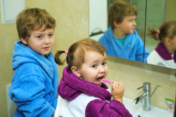 Kinderen poetsen hun tanden 's morgens in de badkamer, gekleed in gewaden — Stockfoto