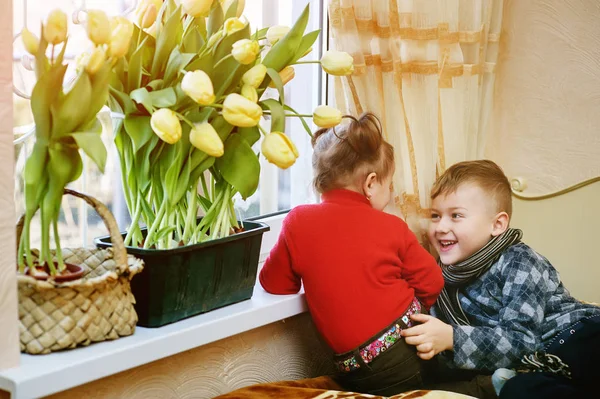 Brat i siostra z kwiatami. Tulipany w oknie — Zdjęcie stockowe