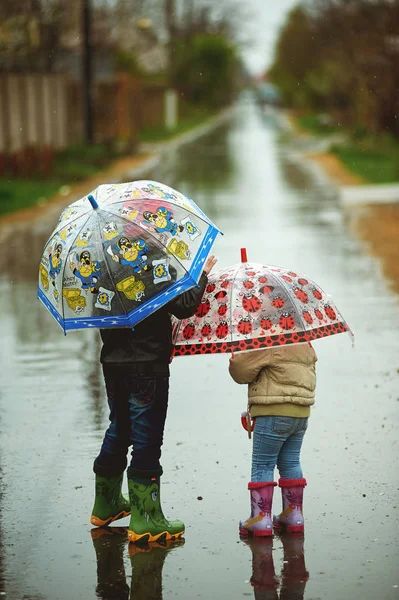 Bruder und Schwester laufen im Regen und halten Regenschirme in der Hand — Stockfoto