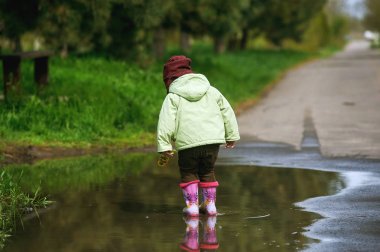 Çocuk çiçek tutan bir su birikintisi içinde ayakta