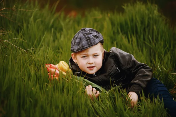 Der Junge auf dem Rasen im Frühling mit einem Blumenstrauß — Stockfoto