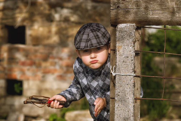 Маленький мальчик в кепке, хулиган с рогаткой в руках
