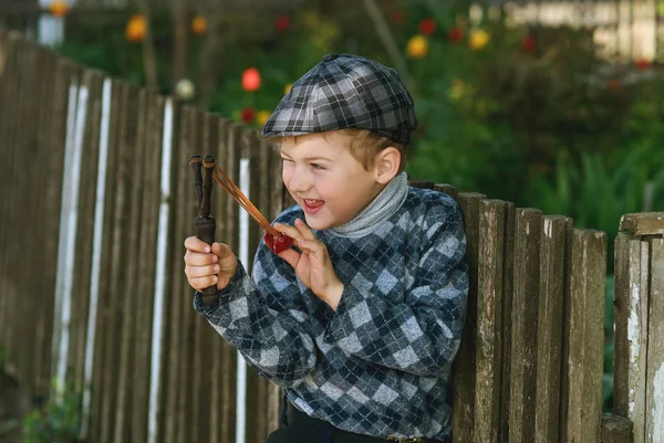 टोपी में छोटा लड़का, हाथों में एक स्लिंगशॉट के साथ धौंसियाना — स्टॉक फ़ोटो, इमेज