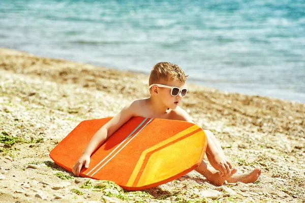 Niño feliz en la playa con una tabla de surf. El concepto de vacaciones de verano —  Fotos de Stock