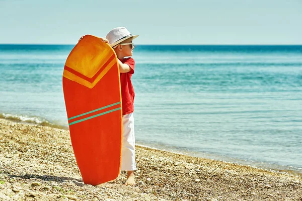 Niño feliz en la playa con una tabla de surf. El concepto de vacaciones de verano — Foto de Stock