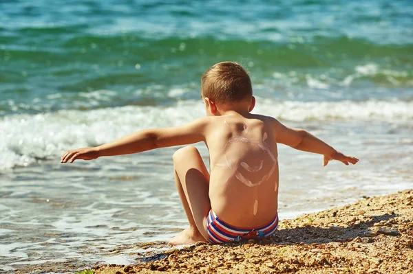 Widok z tyłu chłopca na morzu ciesząc się słońcem na plaży. Ochrony przeciwsłonecznej — Zdjęcie stockowe