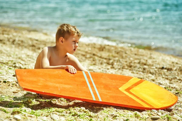 Szczęśliwy chłopiec na plaży z deski surfingowej. Koncepcja lato wakacje — Zdjęcie stockowe