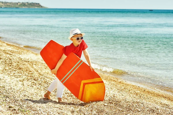 Niño feliz en la playa con una tabla de surf. El concepto de vacaciones de verano — Foto de Stock