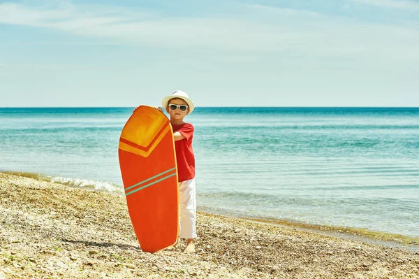 Niño feliz en la playa con una tabla de surf. El concepto de vacaciones de verano — Foto de Stock