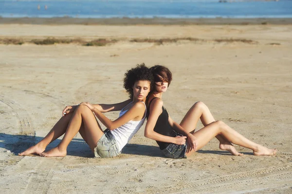 Twee meisjes model poseren liggend op het zand. Het concept van zomer kleding — Stockfoto