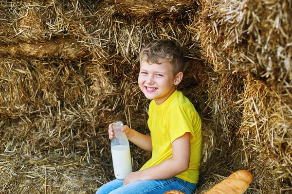 boy drinking milk from a bottle on the background of hay on the farm.