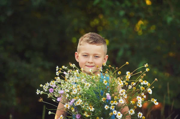 Портрет веселого мальчика на природе с букетом полевых цветов — стоковое фото