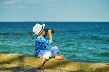 Bir çocuk sahilde dürbün ile yürür.