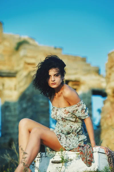 Schöne junge Modell Mädchen im Sommerkleid sitzt in Retro-Koffer auf dem Hintergrund eines alten Gebäudes . — Stockfoto