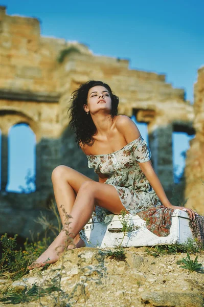 Güzel genç model kız retro çanta eski bir bina bir arka plan üzerinde oturan yaz elbise .