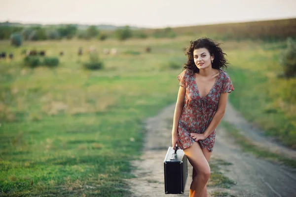 Beautiful young model girl in a summer dress in a field on a dirt road — Stock Photo, Image