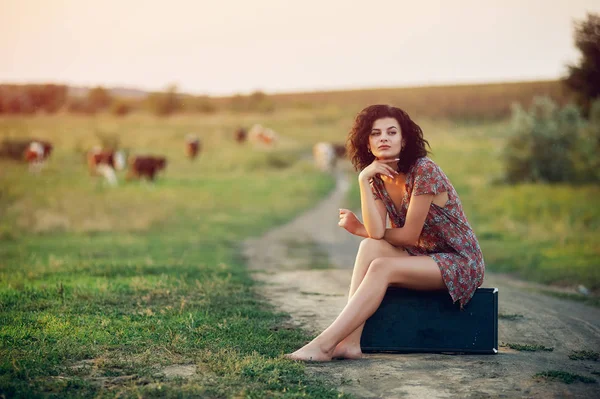 Mooie jonge model meisje in een zomerjurk in een veld op een onverharde weg — Stockfoto