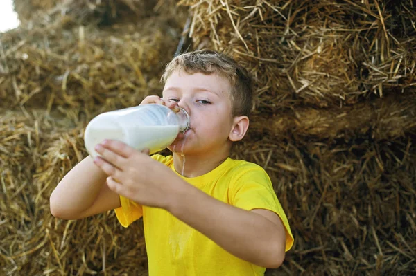 boy drinking milk from a bottle on the background of hay on the farm