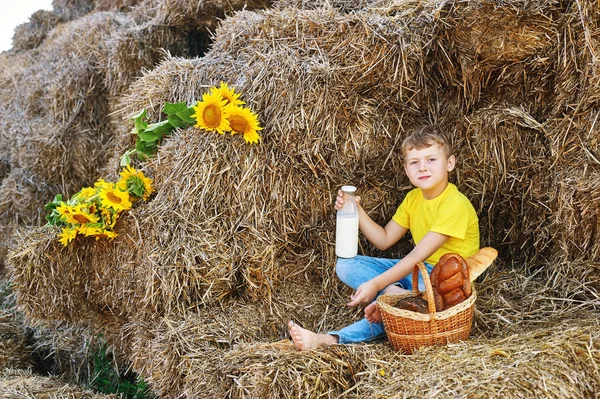 Niño beber leche de una botella en el fondo de heno en la granja . — Foto de Stock