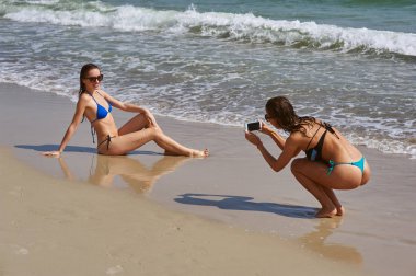 Eğlenceli deniz kenarında iki genç kadın, o onun kız arkadaşı bir cep telefonu alır