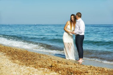 Gelin ve damat ayakta kol kola sahilde