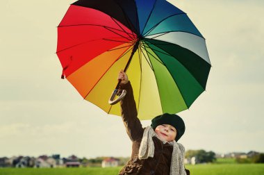 Yeşil çayır üzerinde renkli bir şemsiye altında duran çocuk, 