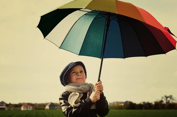 Das Kind, das unter einem bunten Regenschirm auf der grünen Wiese steht — Stockfoto