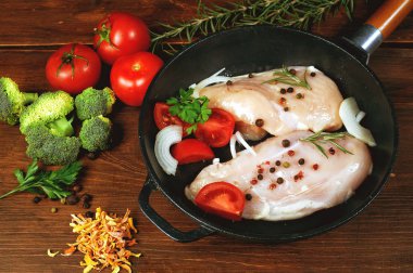 Bir dökme demir tavada sebze malzemelerle çiğ tavuk göğsü. Pişirme