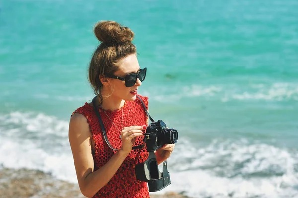 Joven mujer elegantemente vestida con una vieja cámara en la orilla del mar — Foto de Stock