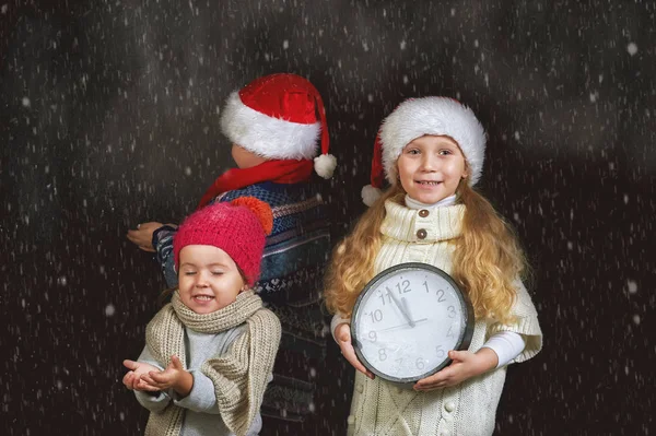 Діти з годинником і різдвяним капелюхом на темному тлі — стокове фото