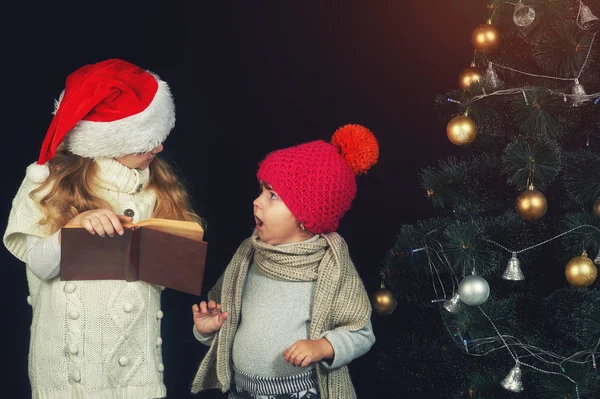 Cute little children reading a book by the Christmas tree — Stock Photo, Image
