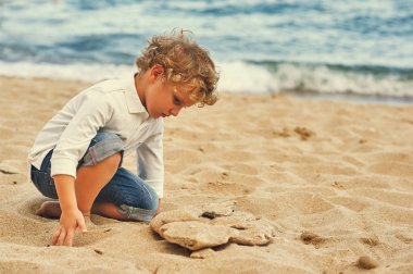 Çocuk kumsalda kumla oynuyor.